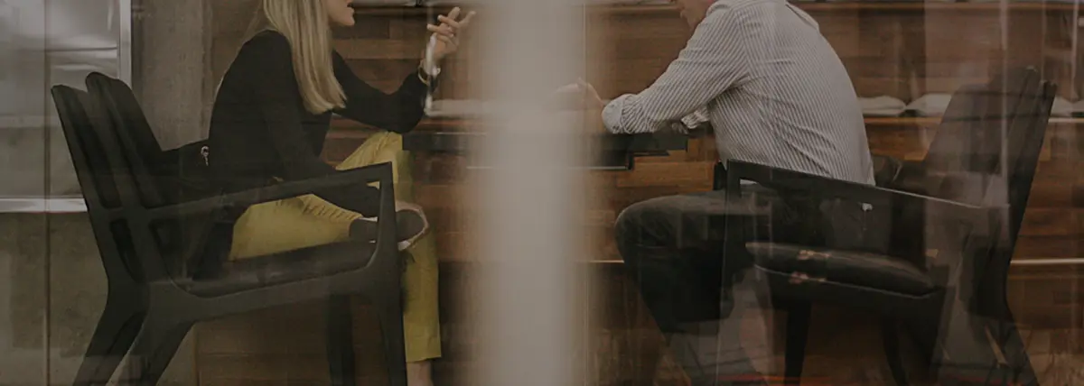 a photo of two people talking at a table surreptitiously taken from outside the room