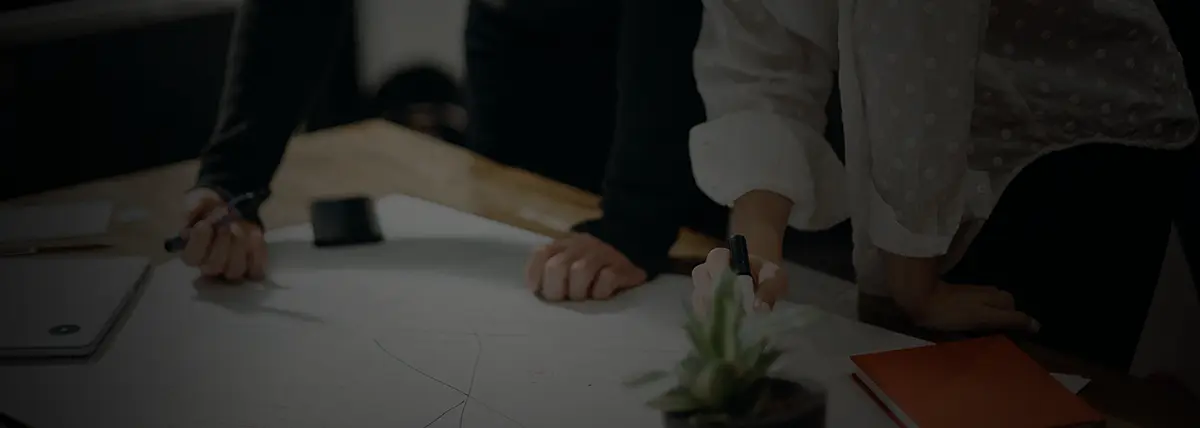 two people looking down at a diagram on a desk while one person writes on it