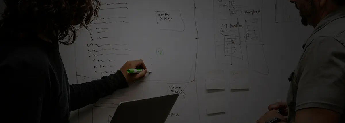 two people looking at a white-board while one person writes on it