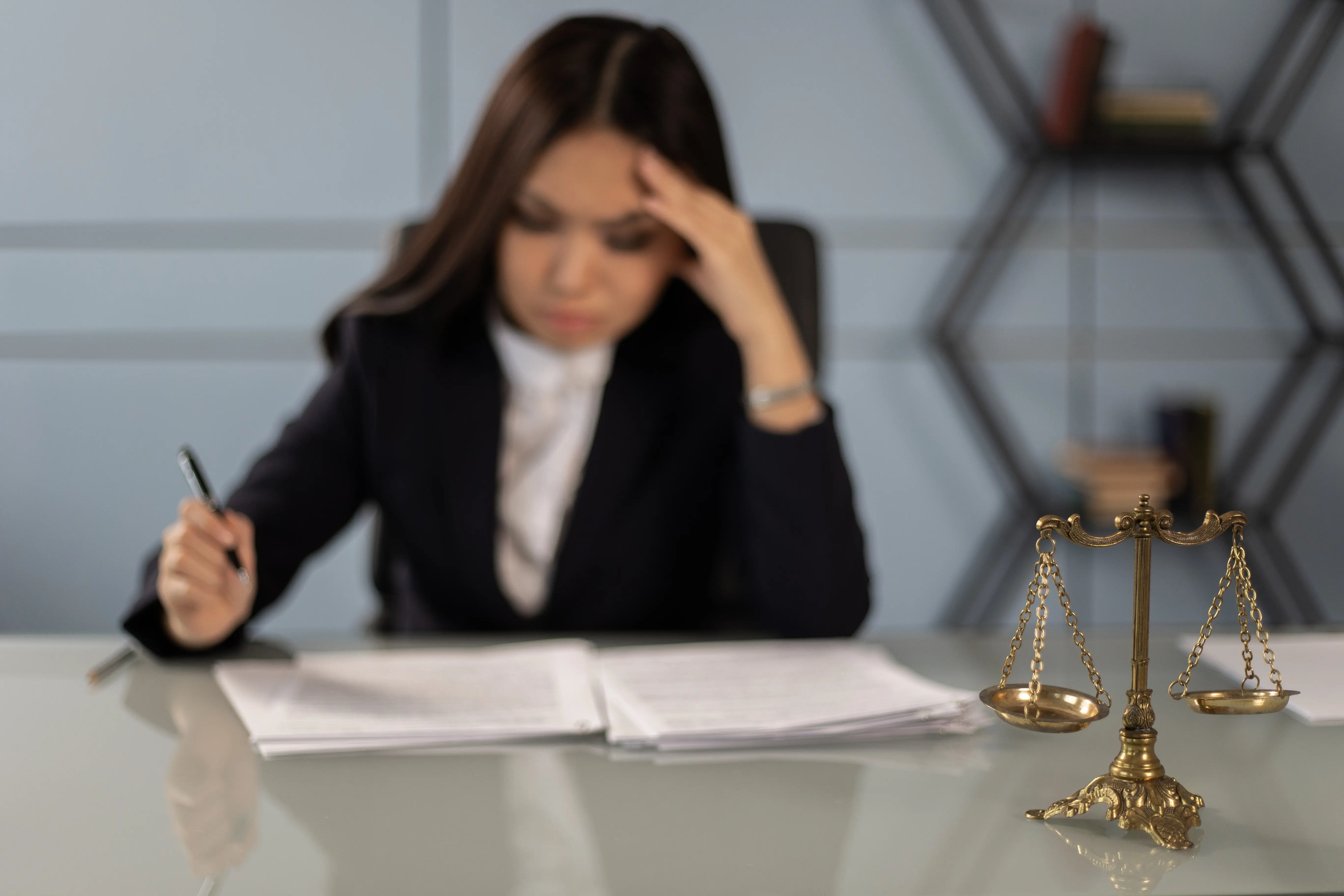 photo of brass scales in the foreground and a woman dressed in business wear working at a desk in the background