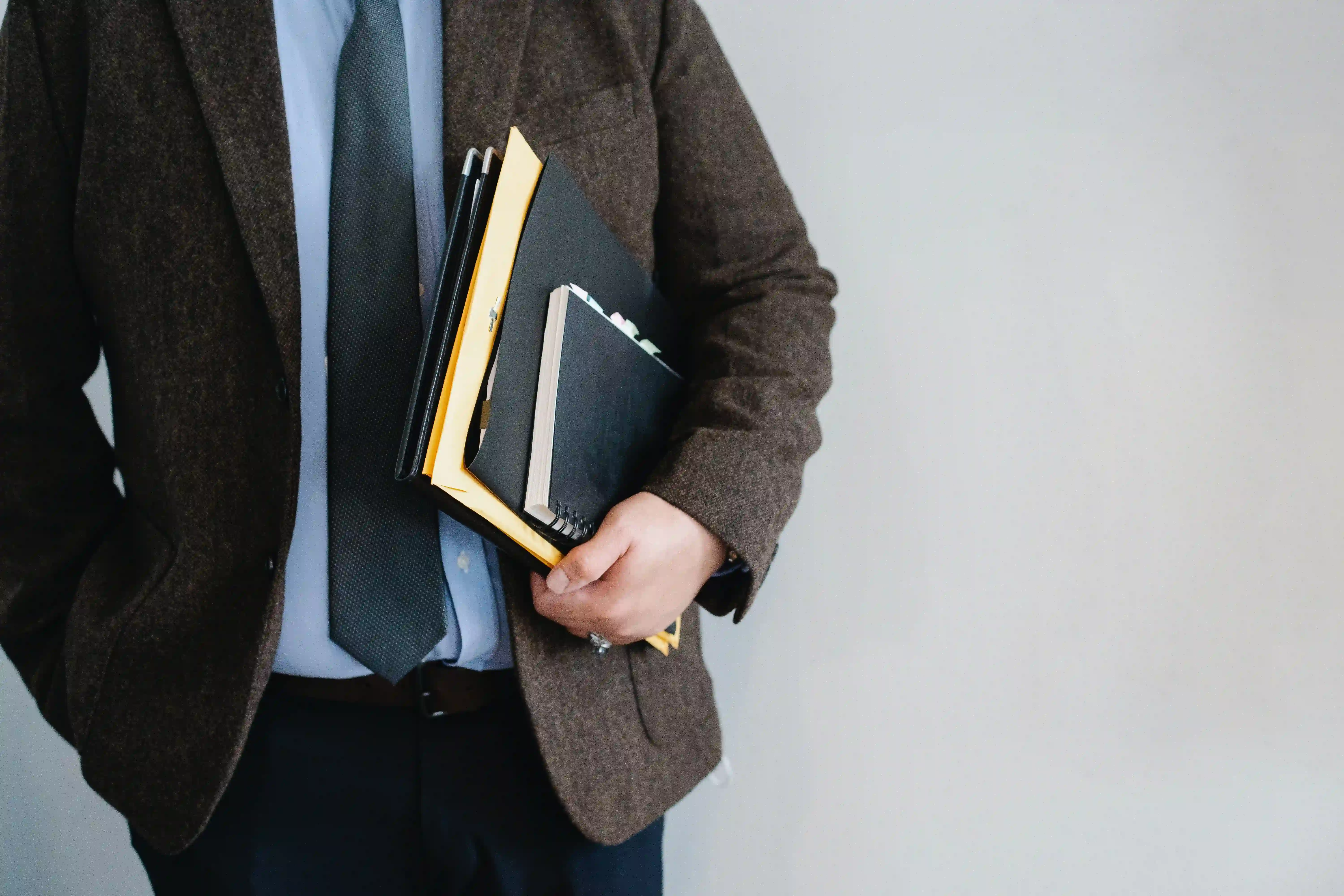 photo of man form upper chest to thigh holding notebooks and wearing a suit